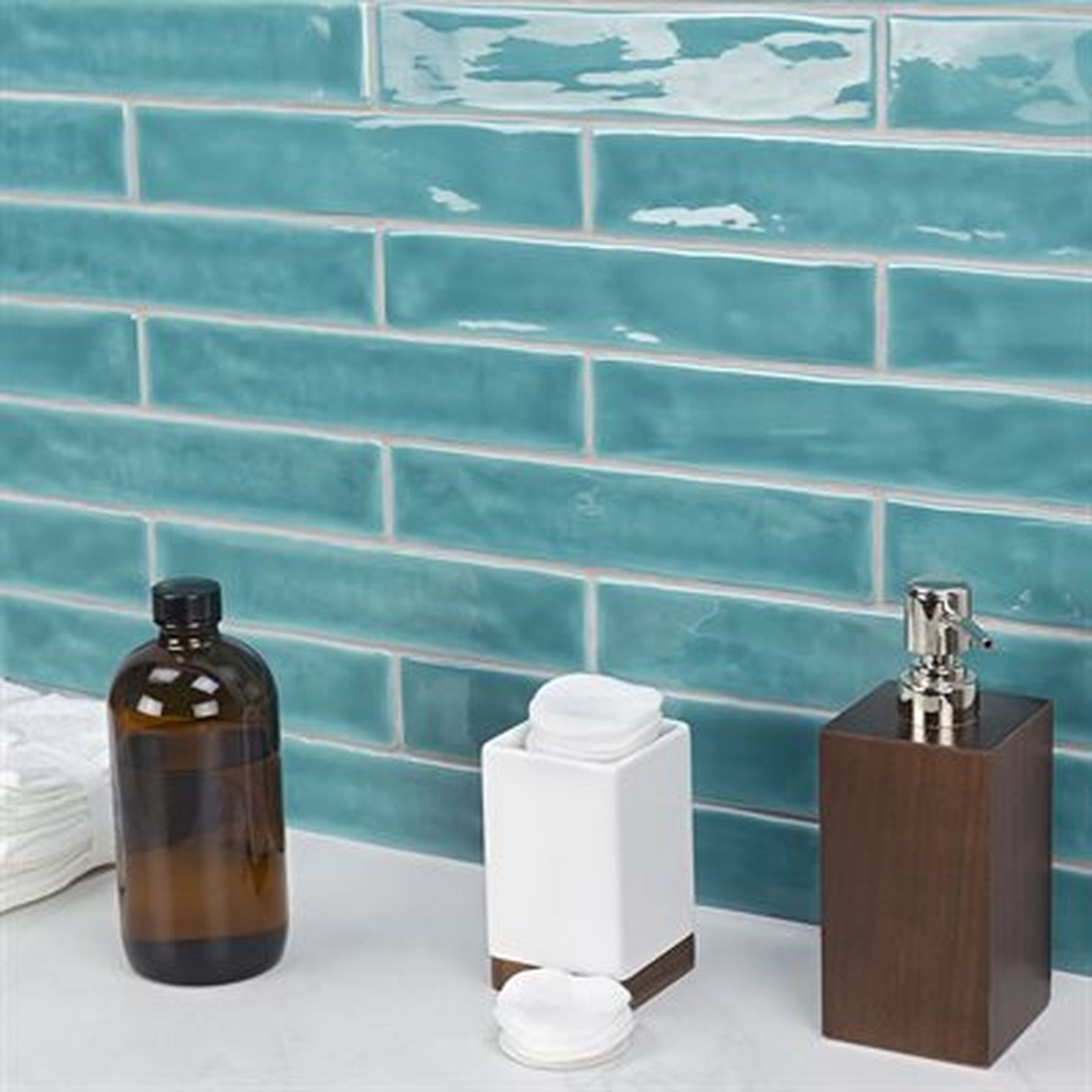 Bathroom counter with teal subway tile, amber bottle, white cotton ball dispenser, and brown soap dispenser.