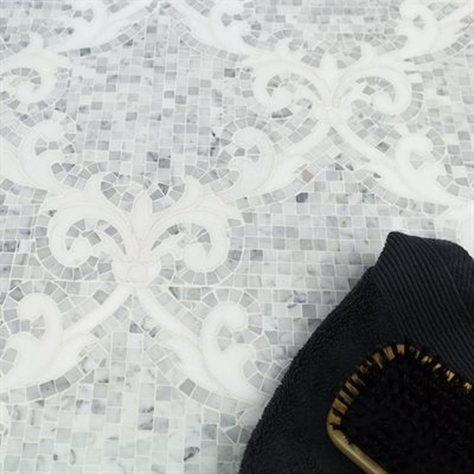 Close-up of white mosaic tile floor with a black towel and brush in the corner.