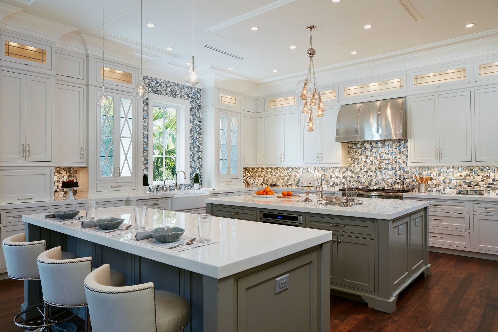 Elegant white kitchen with gray islands, white cabinets, decorative backsplash, and dark wood floors.