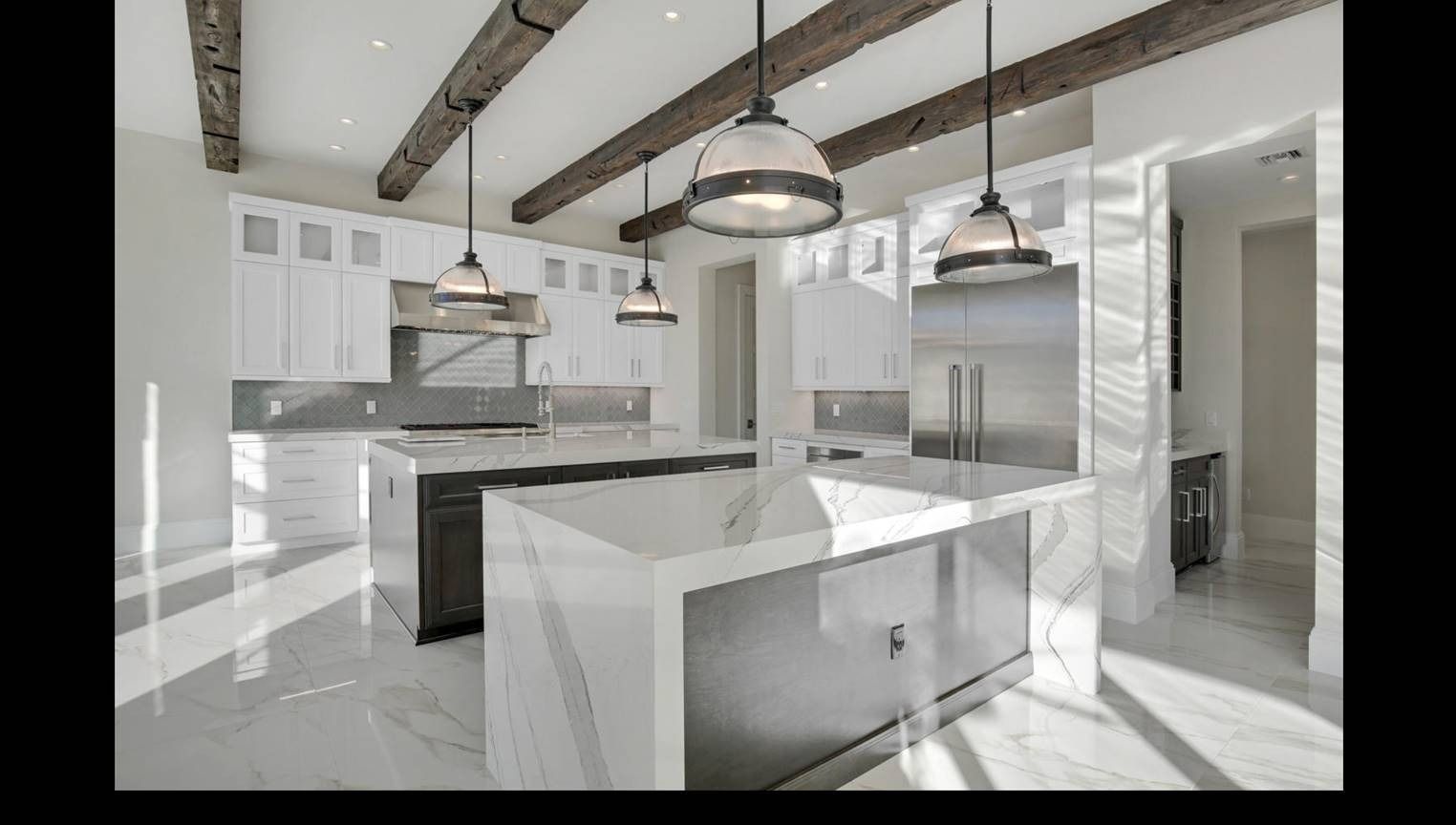 Bright kitchen with white cabinets, marble countertops, wooden beams, stainless steel appliances, and two islands.