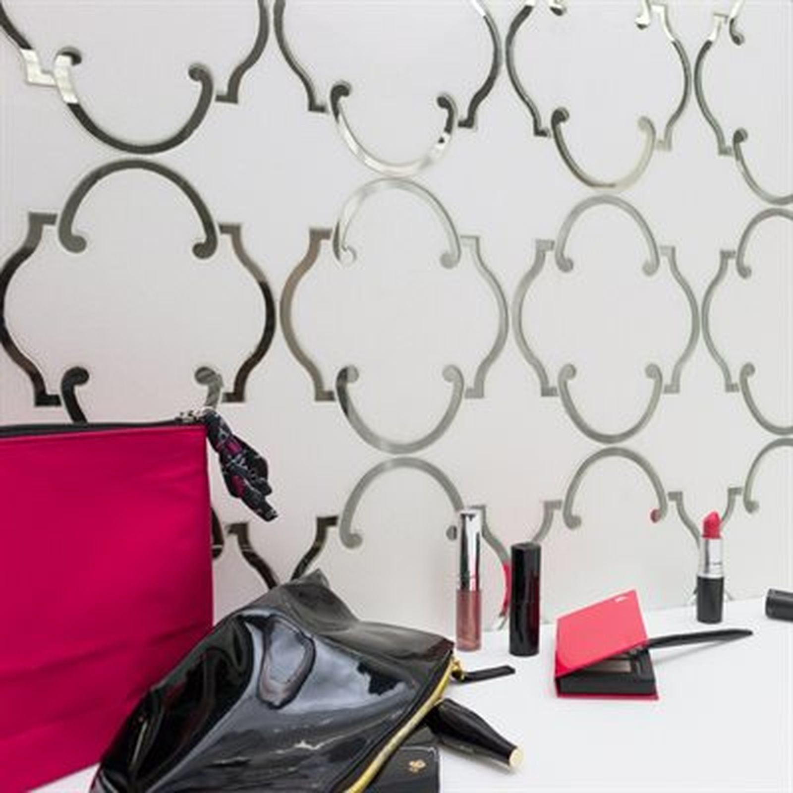 Makeup items and bags on white surface, with silver patterned wall in the background.