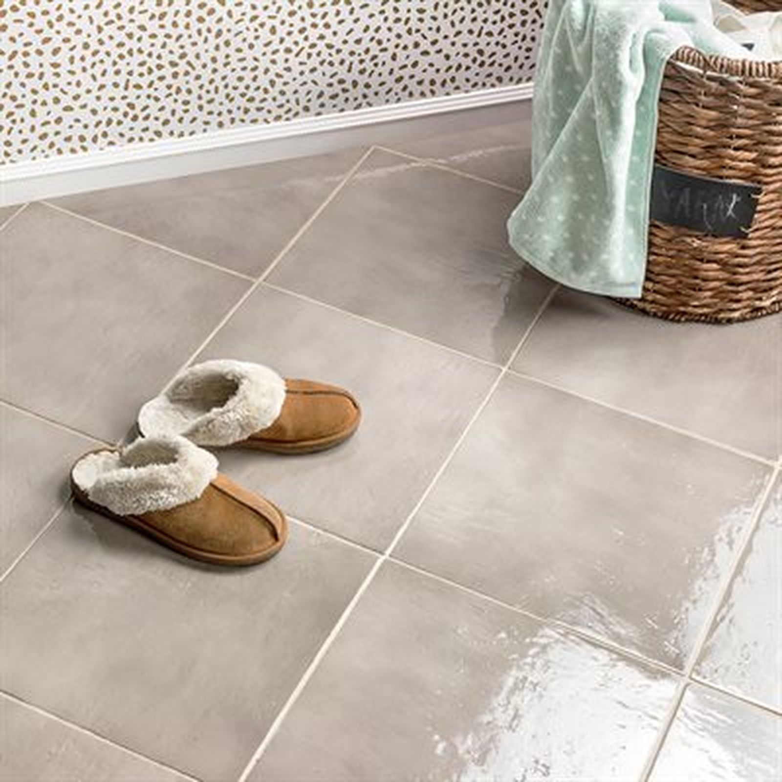 Pair of slippers on tiled floor next to a wicker basket with a towel.
