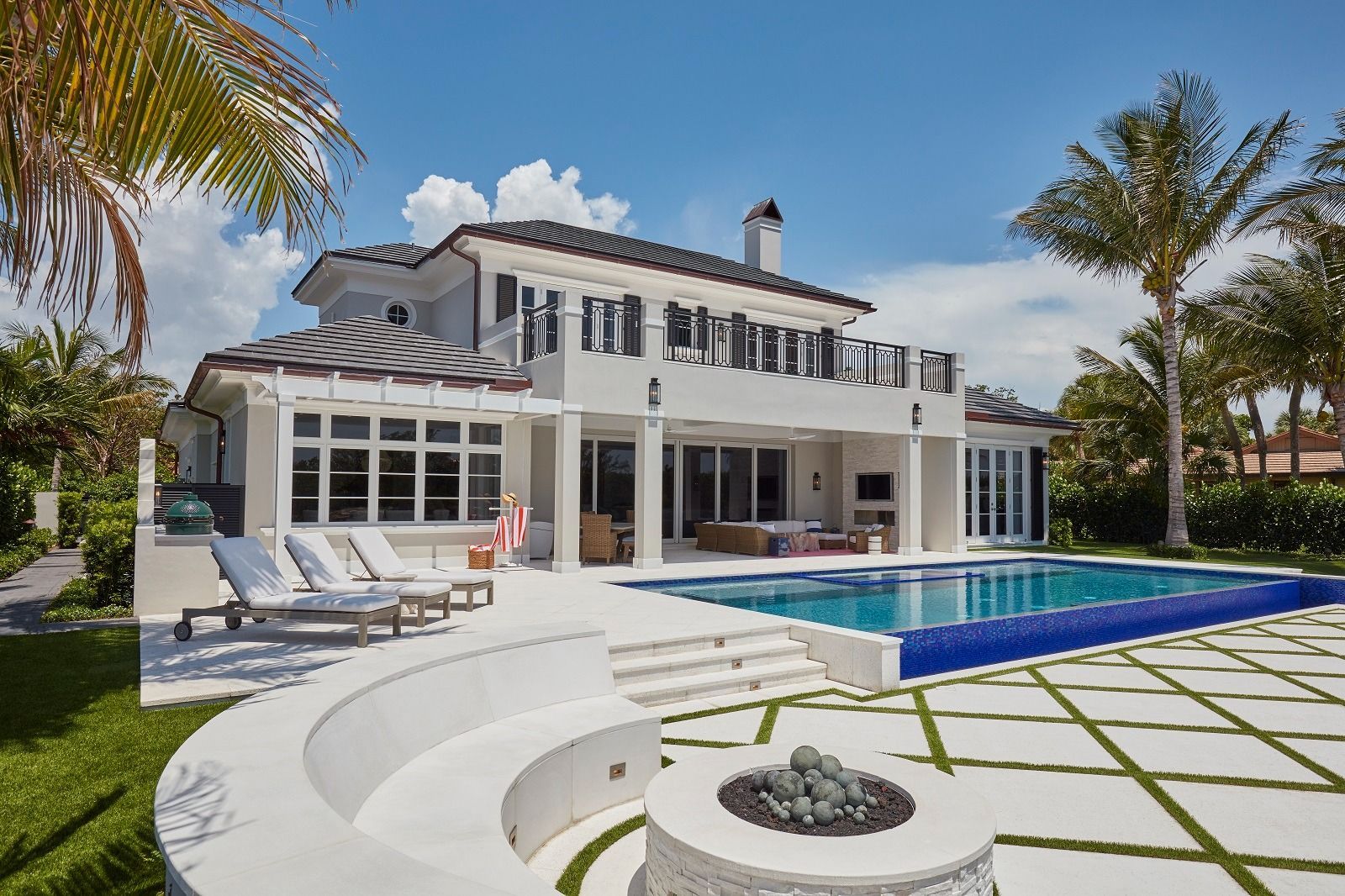 Luxurious white house with a pool, patio, and fire pit in a tropical setting.