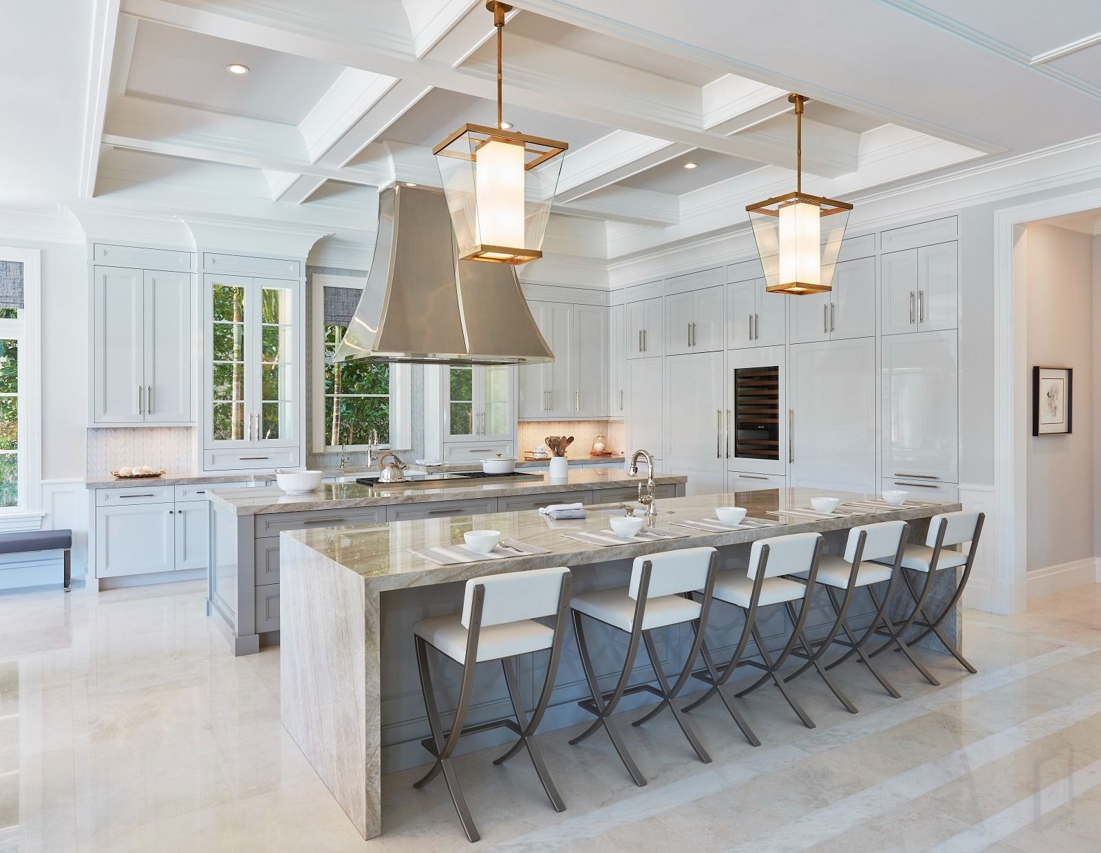Modern white kitchen with two islands, light gray cabinets, and gold pendant lights.