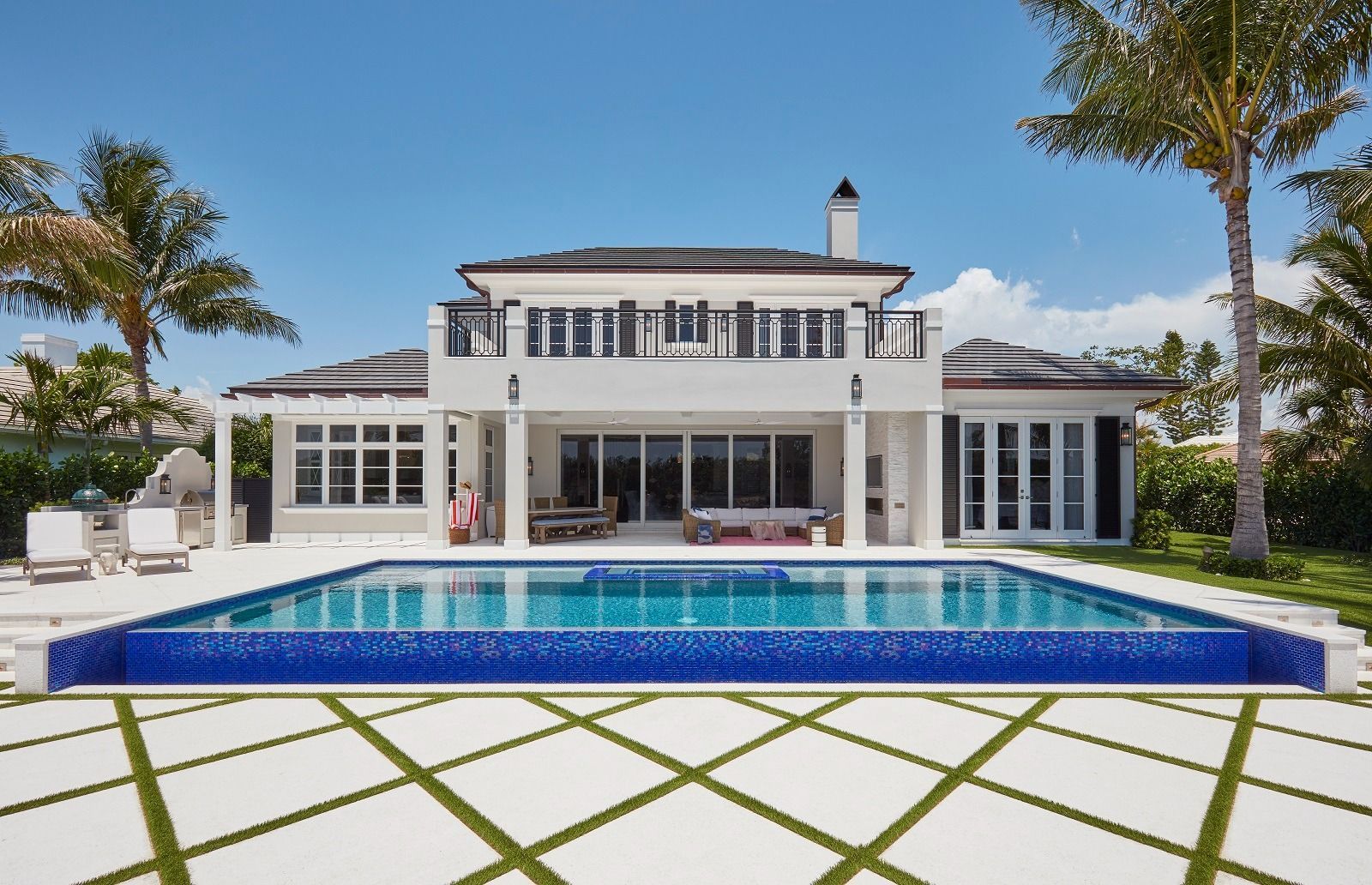 Luxury white house with pool, palm trees, and blue sky.