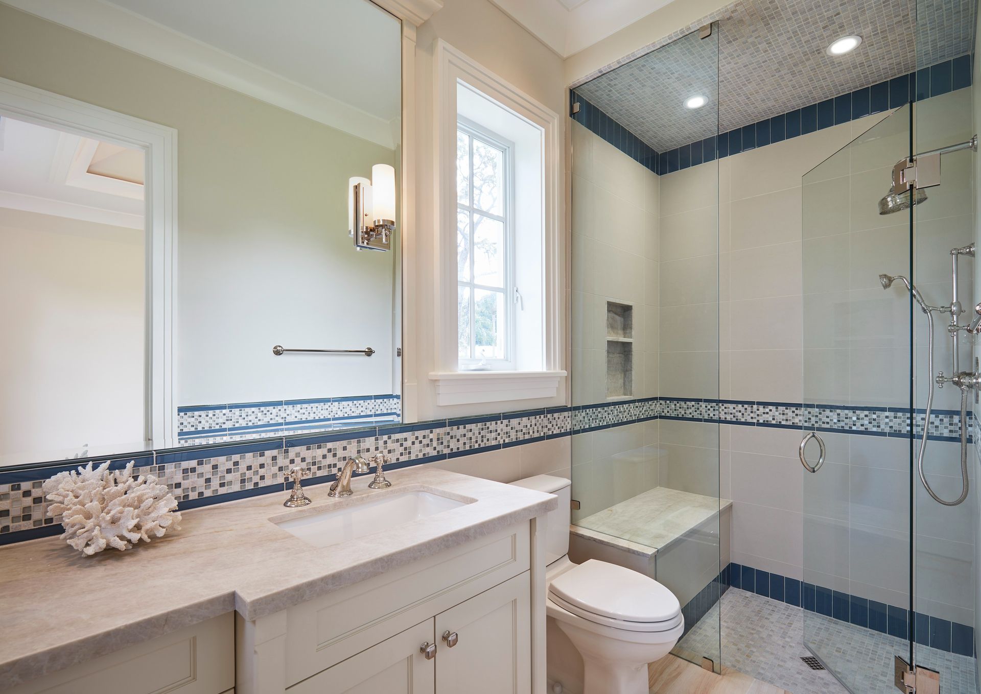 Bathroom with shower, toilet, and vanity. Blue and white tile accents. Large mirror and window.