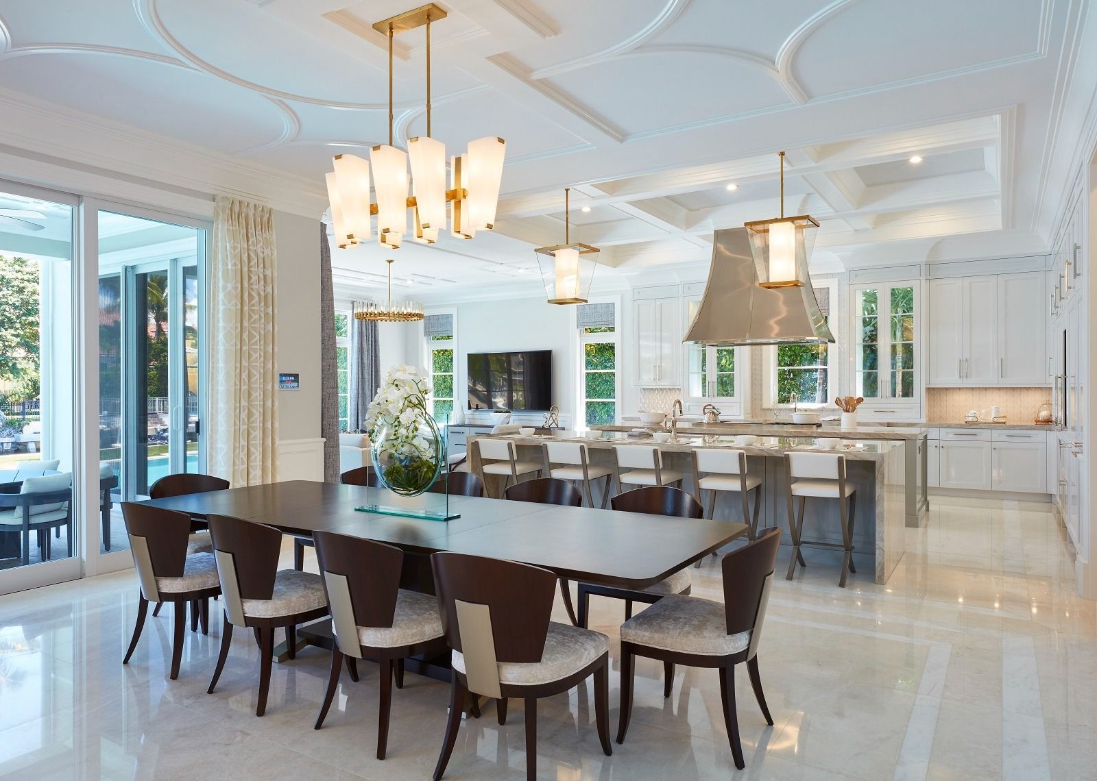 Formal dining room connected to a modern kitchen. Features a large table, chairs, and multiple light fixtures.