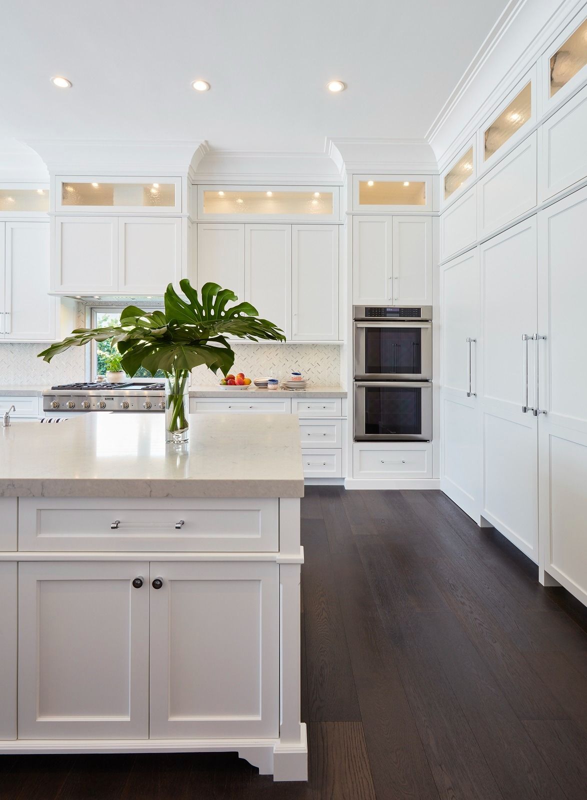 White kitchen with dark wood floors, island, built-in appliances, and overhead lighting.