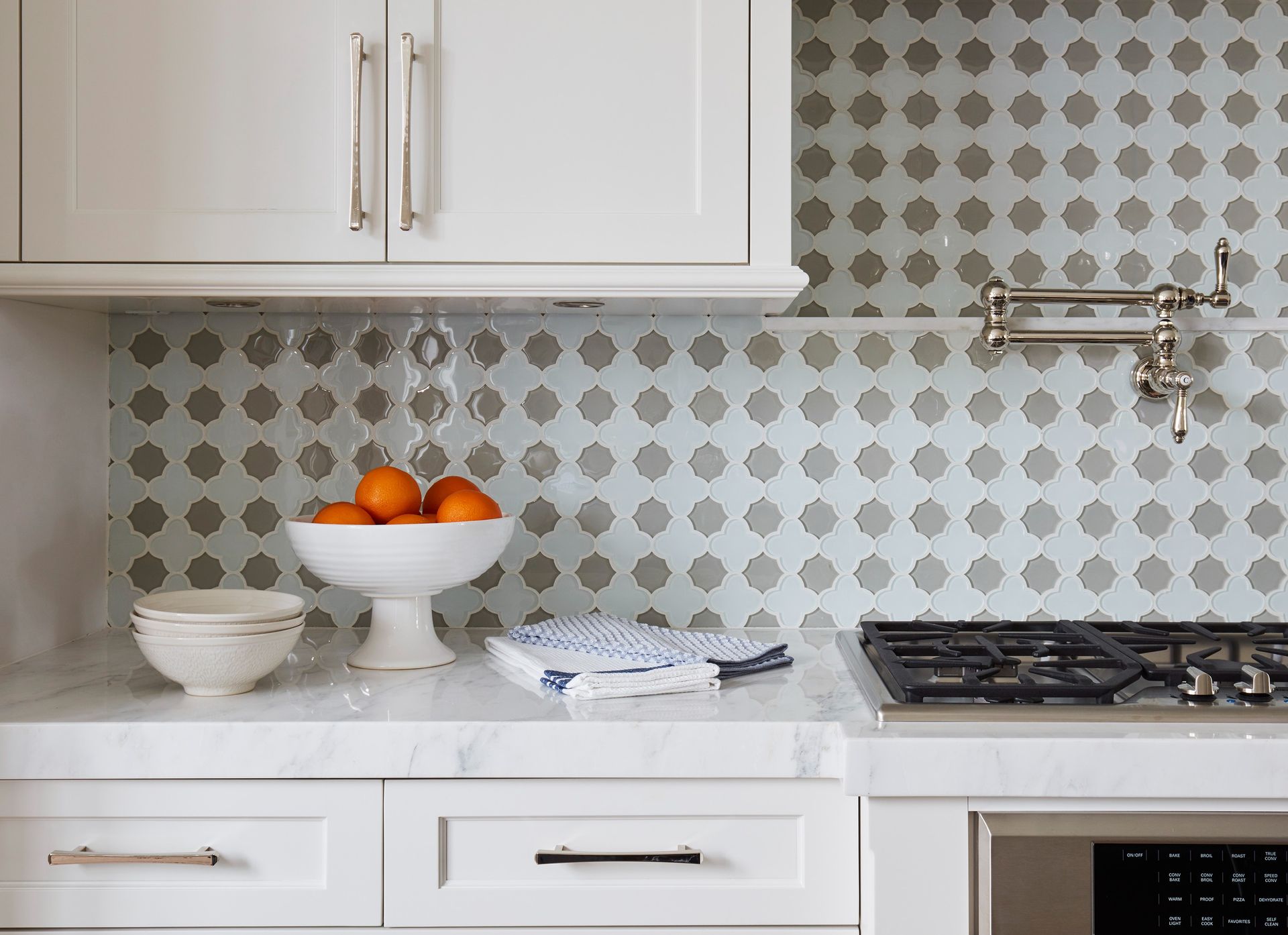 Kitchen with white cabinets, marble countertop, patterned backsplash, and oranges in a bowl.