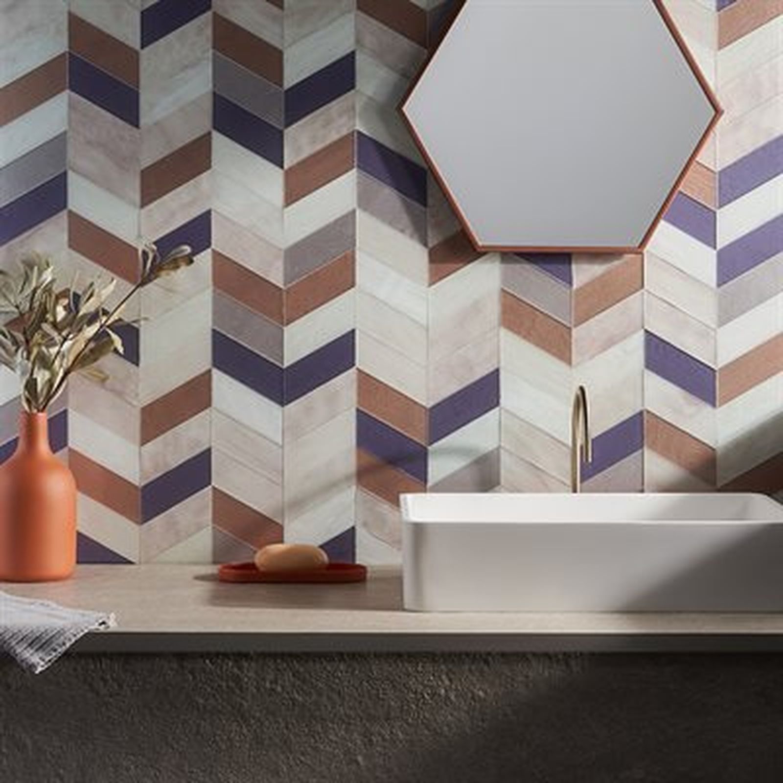 Bathroom with patterned chevron tiles in shades of purple, beige, and brown; white sink, hexagonal mirror.