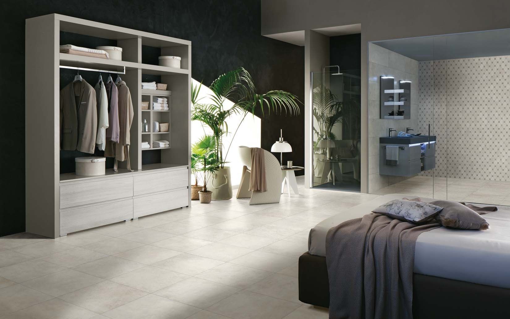 Modern bedroom with open closet, bathroom, and bed. Light floors, dark accent wall, and greenery.