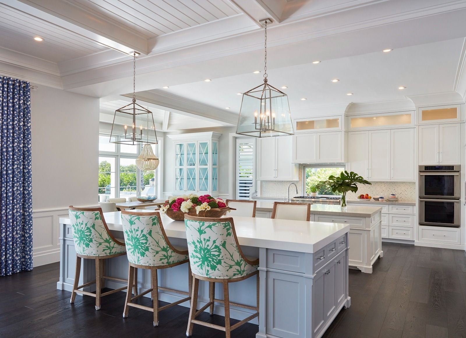Bright kitchen with white cabinets, island, and seating. Floral patterned bar stools and blue drapes.