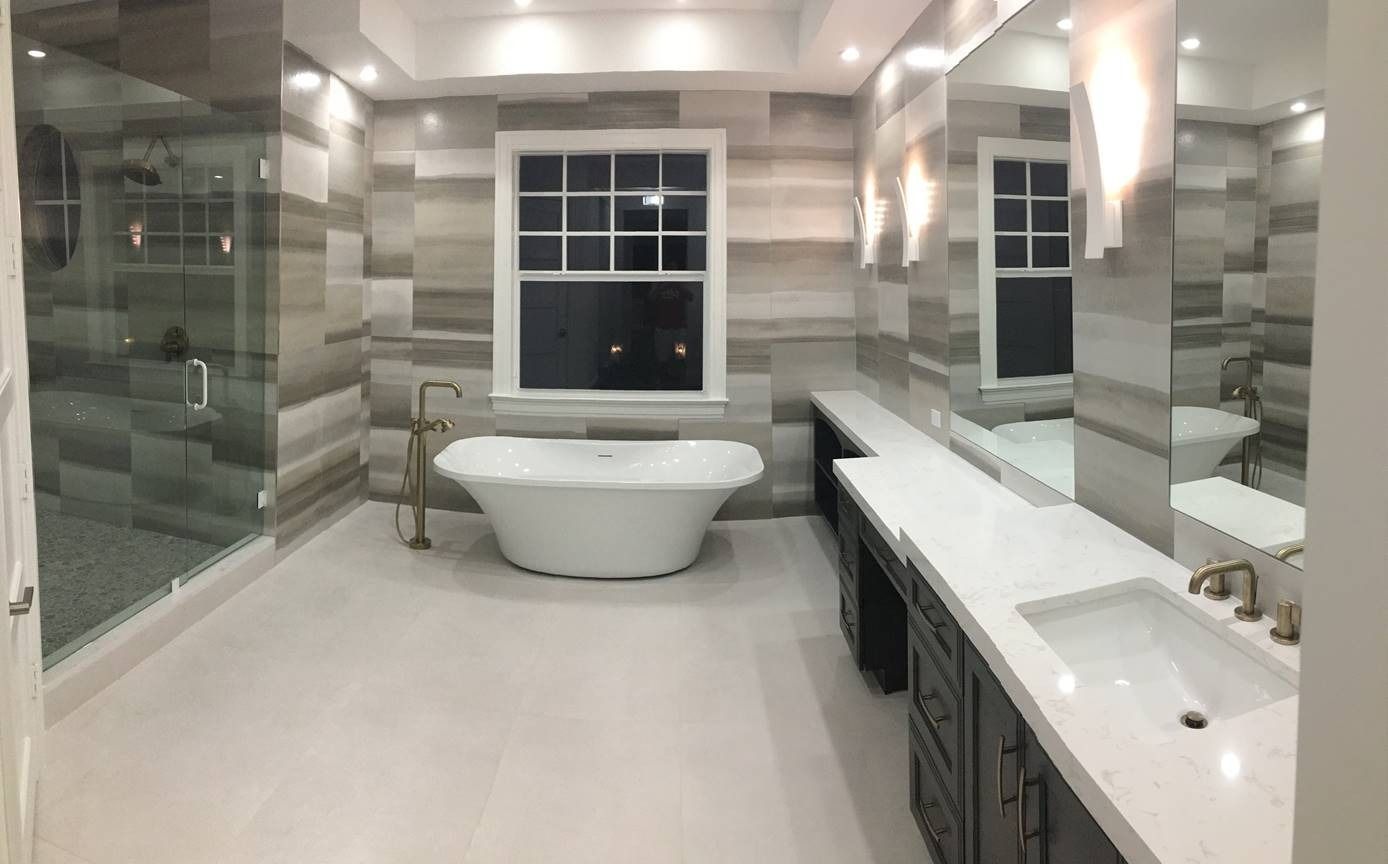 Modern bathroom with a white tub, large window, glass shower, and gray tile walls.