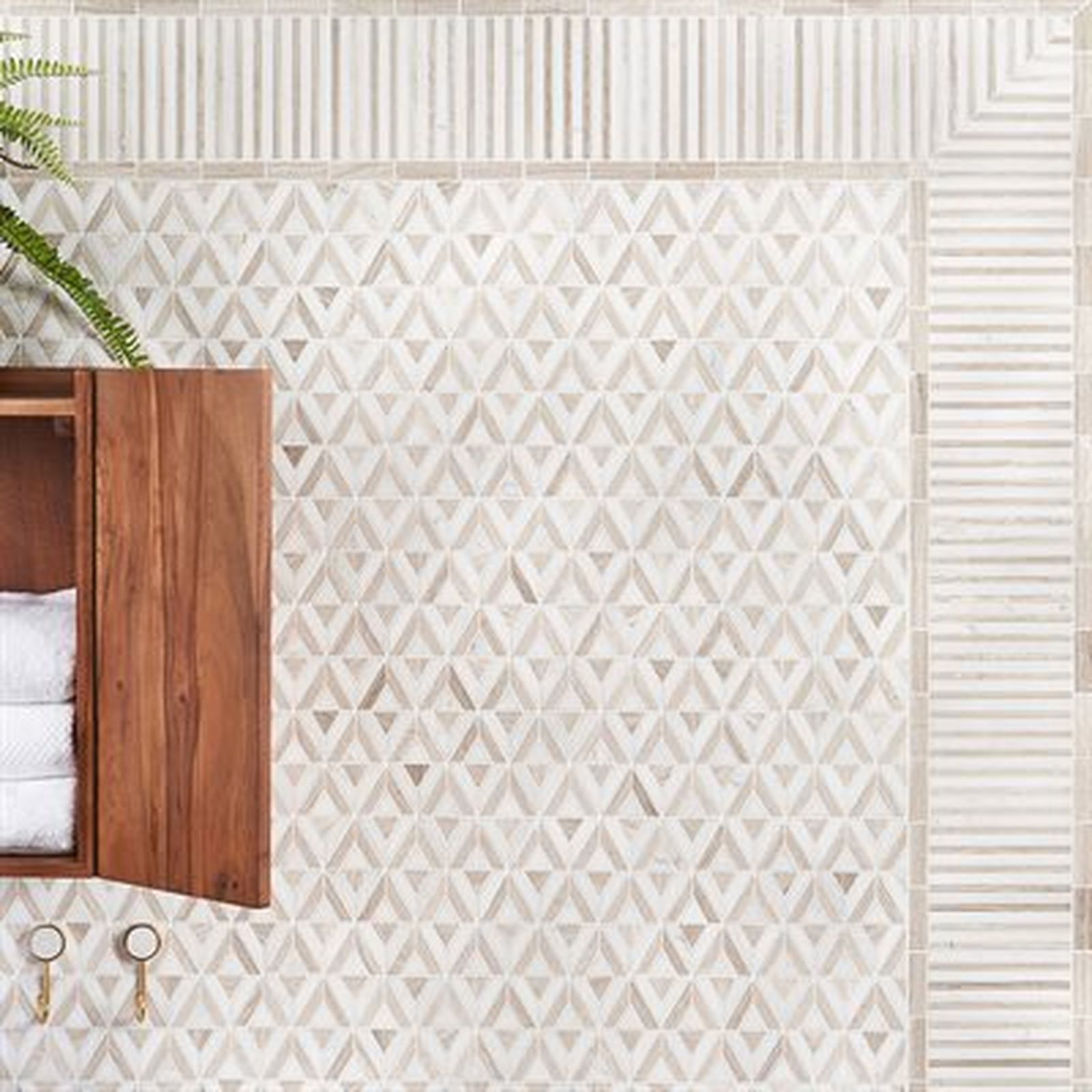 Bathroom with geometric patterned tile and wooden cabinet, towels, and wall hooks.