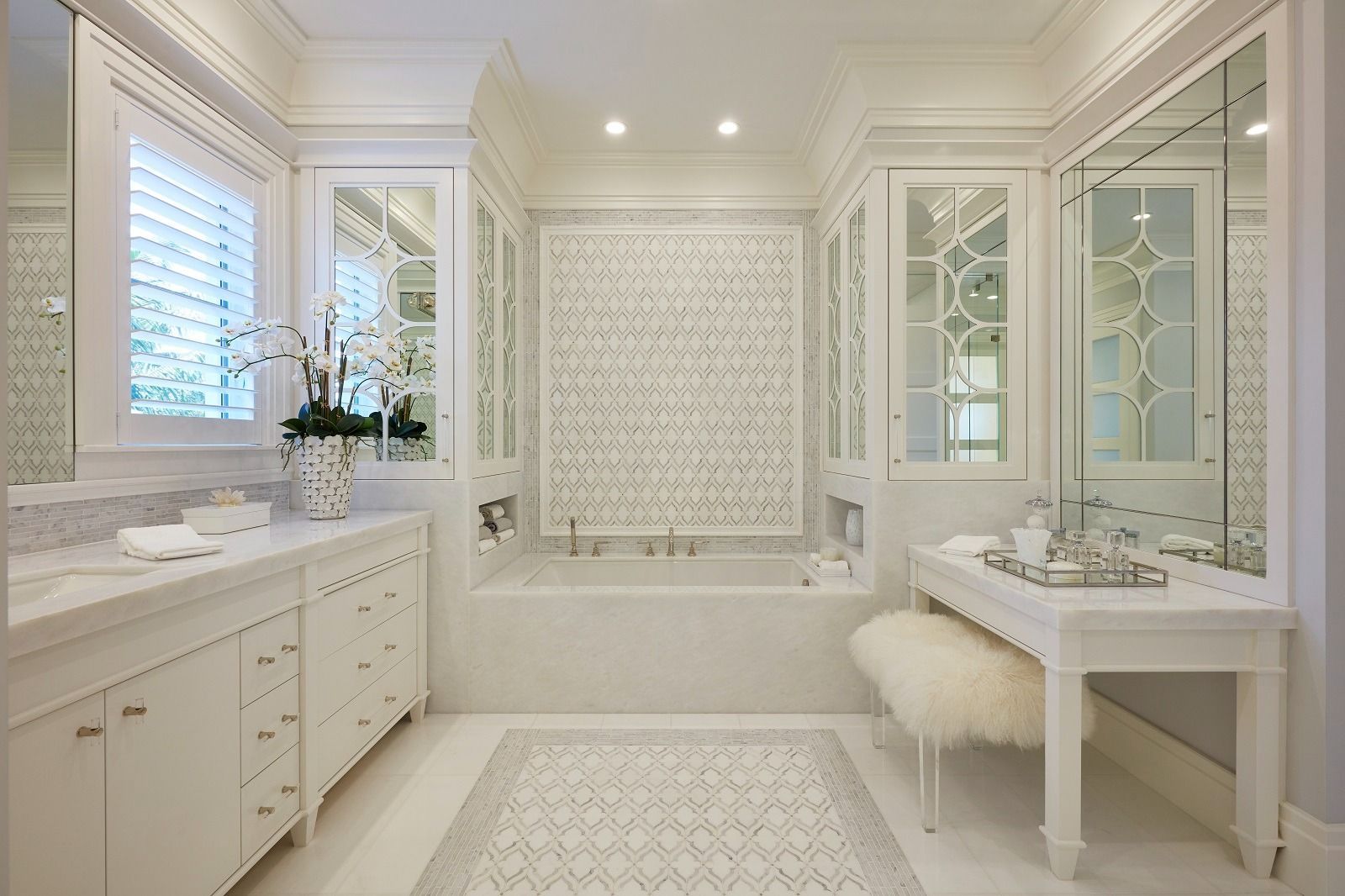 Elegant white bathroom with marble counters, ornate cabinets, tub, and decorative patterned tile.