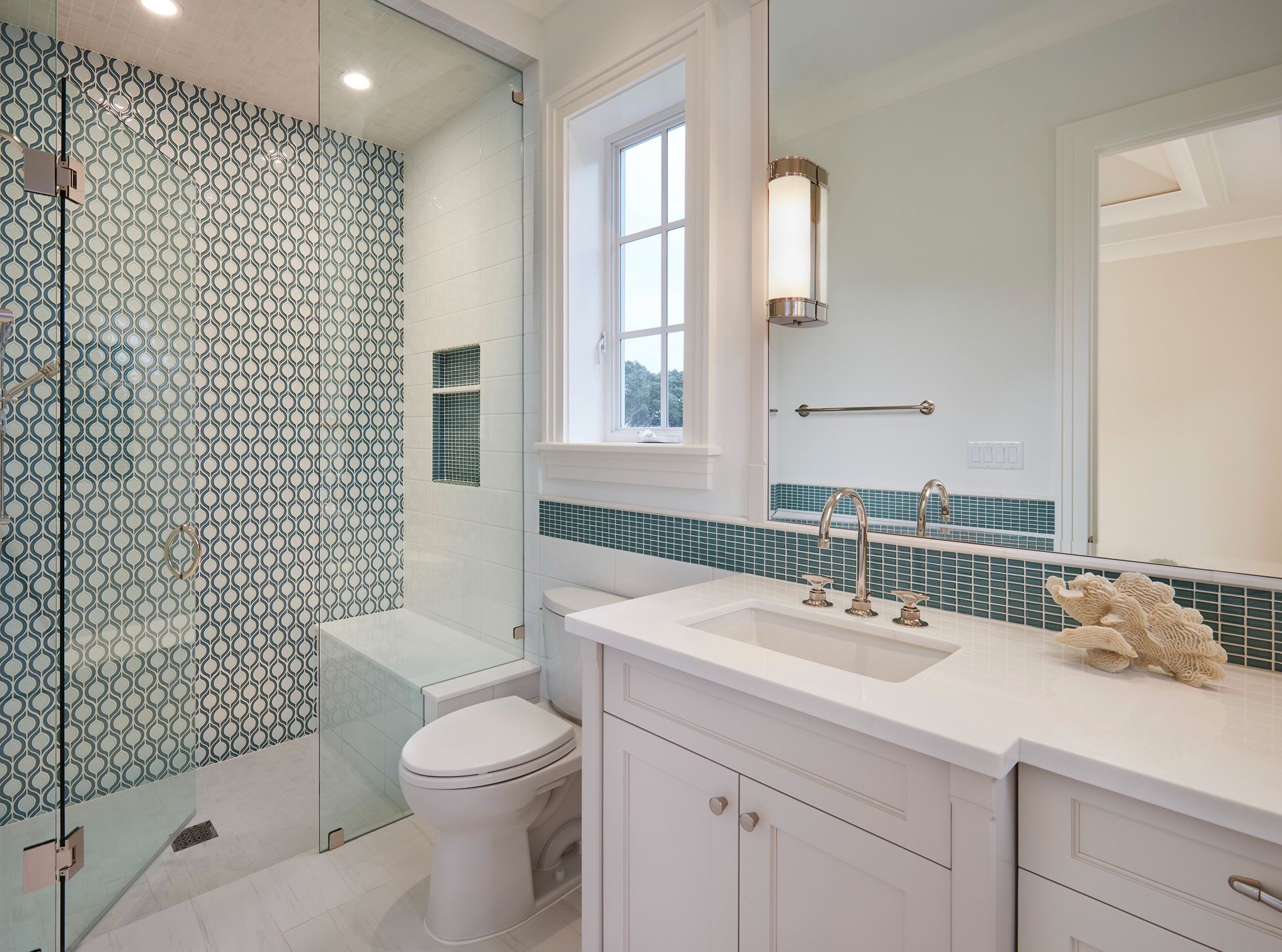 Bathroom with blue tile shower, white vanity, and small window.