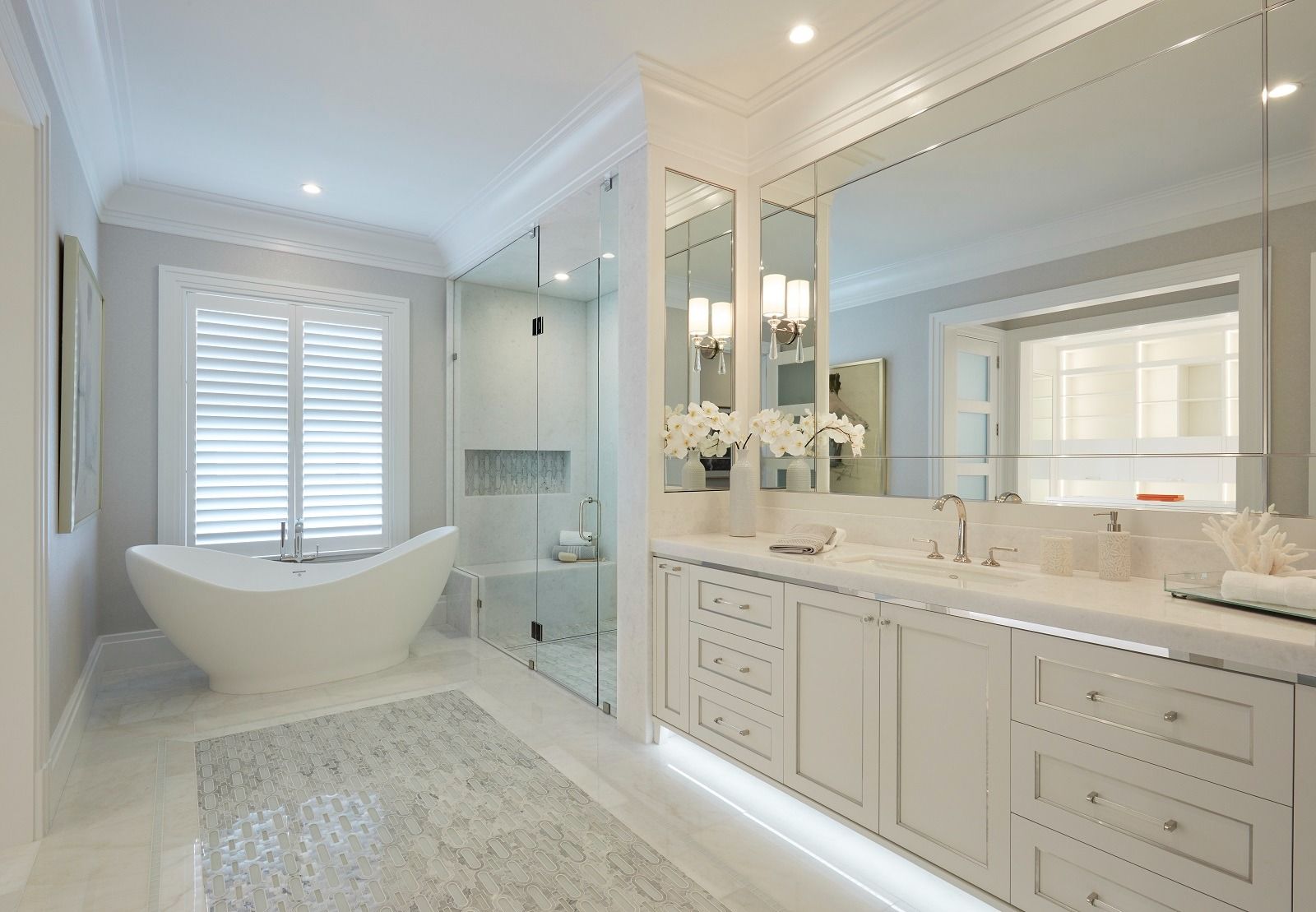 Bright white bathroom with a large bathtub, glass shower, and vanity with mirrors.
