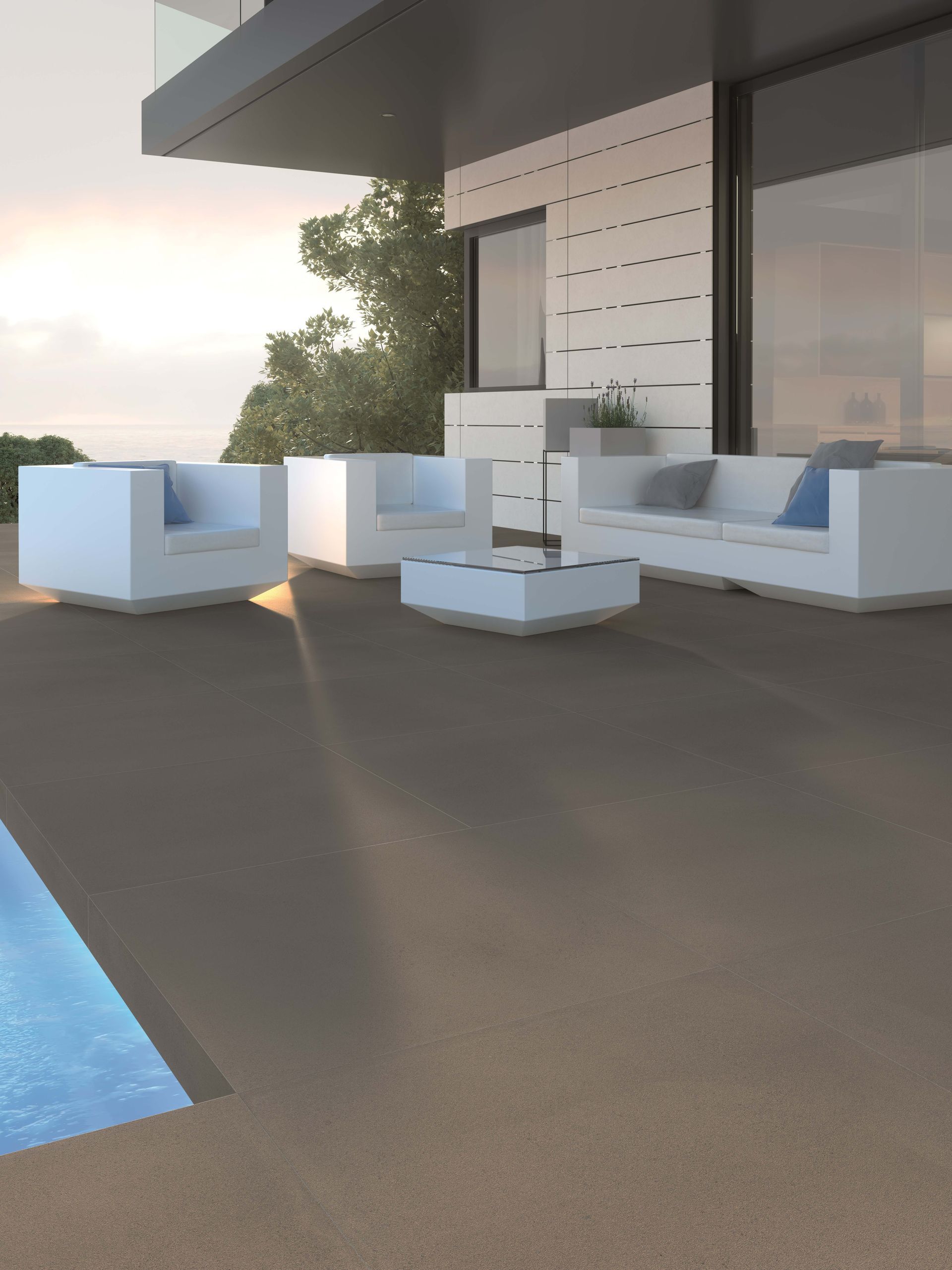 Modern outdoor living space with white furniture, overlooking a pool and the ocean at sunset.