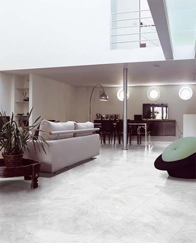Modern living room with white walls, gray floor, sofa, dining area, and round windows.