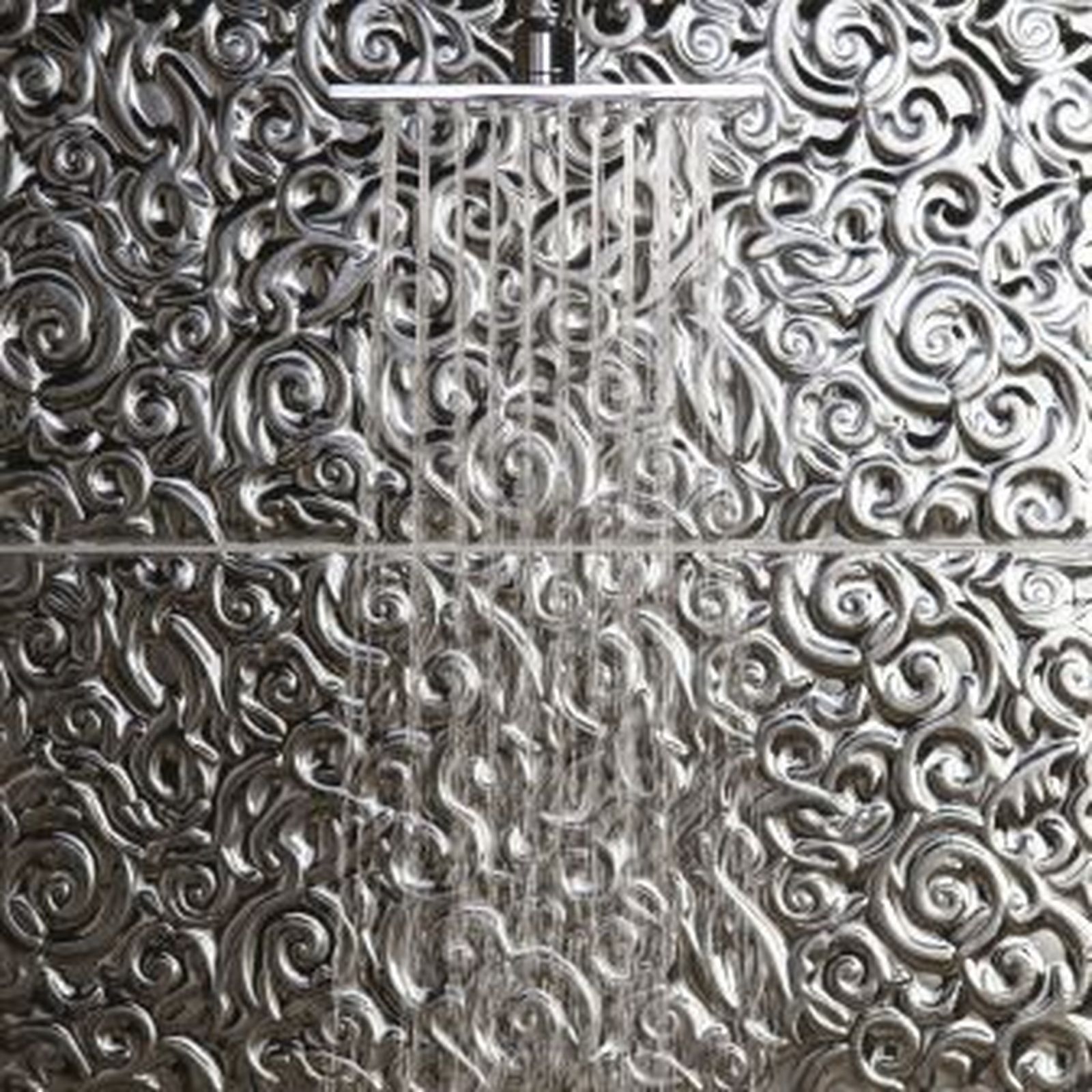 Shower with water streaming against ornate, embossed metallic wall.