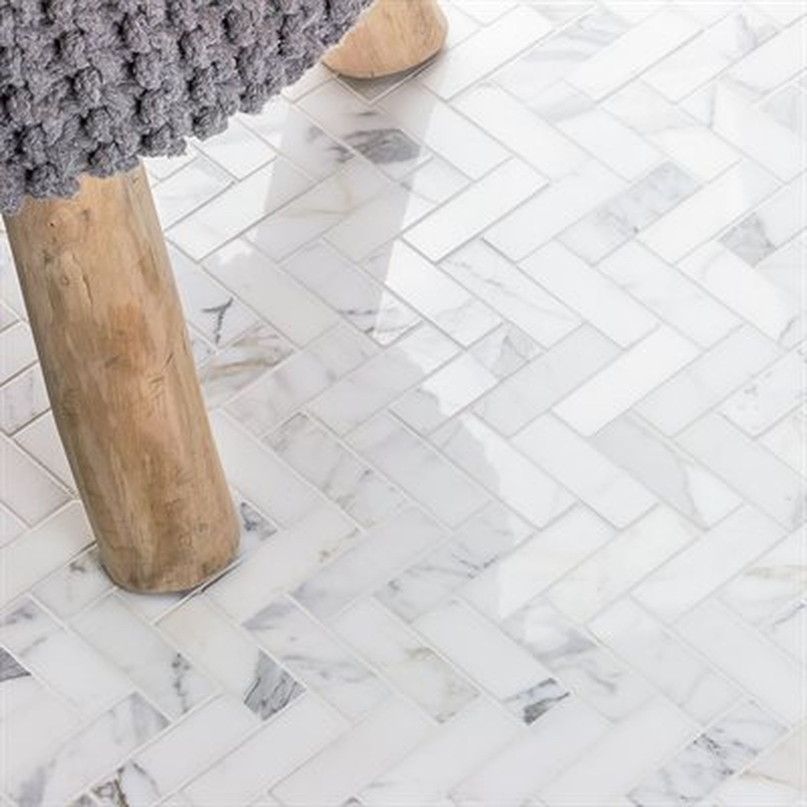 Herringbone marble tile floor with a wooden chair leg and a gray fabric.