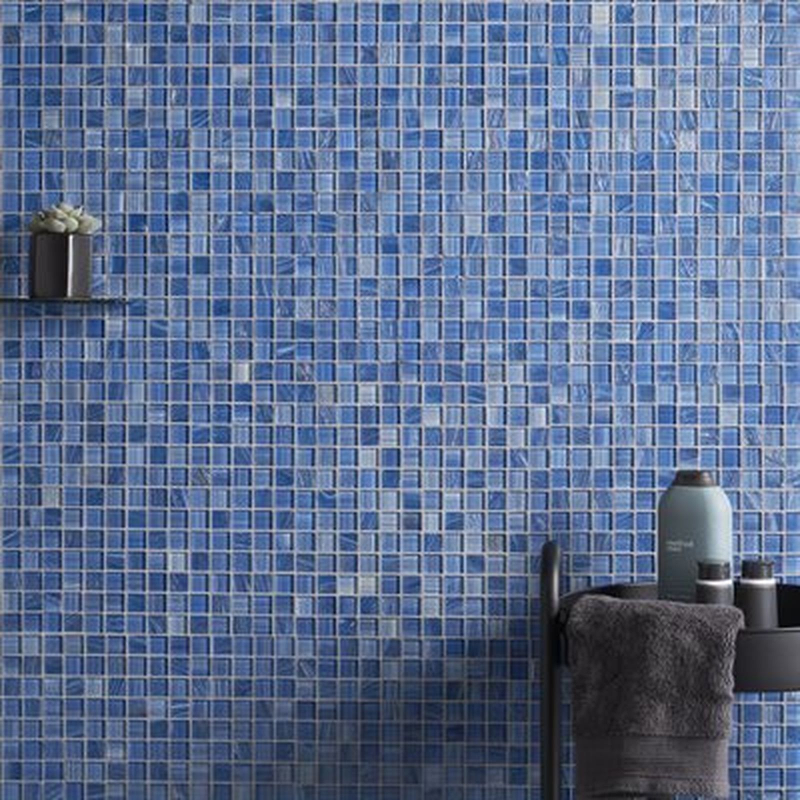 Blue mosaic tile wall with a shelf and toiletries. A towel is hanging below.