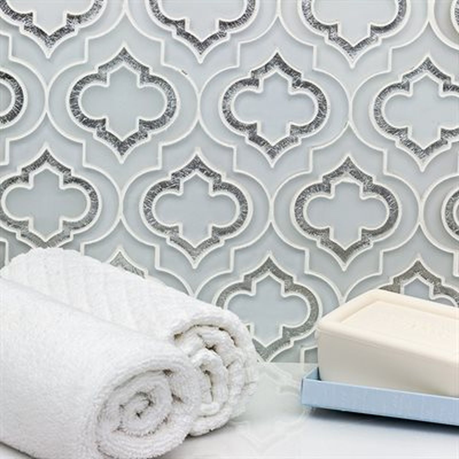 Rolled white towels and soap on a light blue tray sit in front of a patterned tile backsplash.