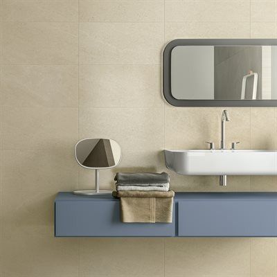 Bathroom with a blue floating cabinet, white sink, and beige tile walls. Features a mirror and towels.