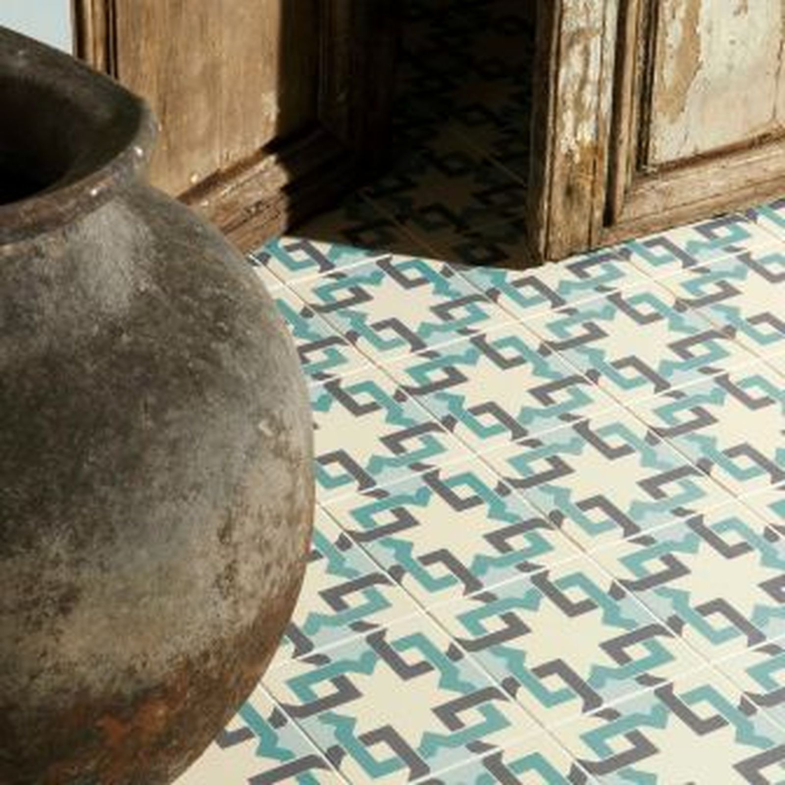 Textured ceramic floor tiles with a blue and gray geometric pattern. A large, dark clay pot sits nearby.