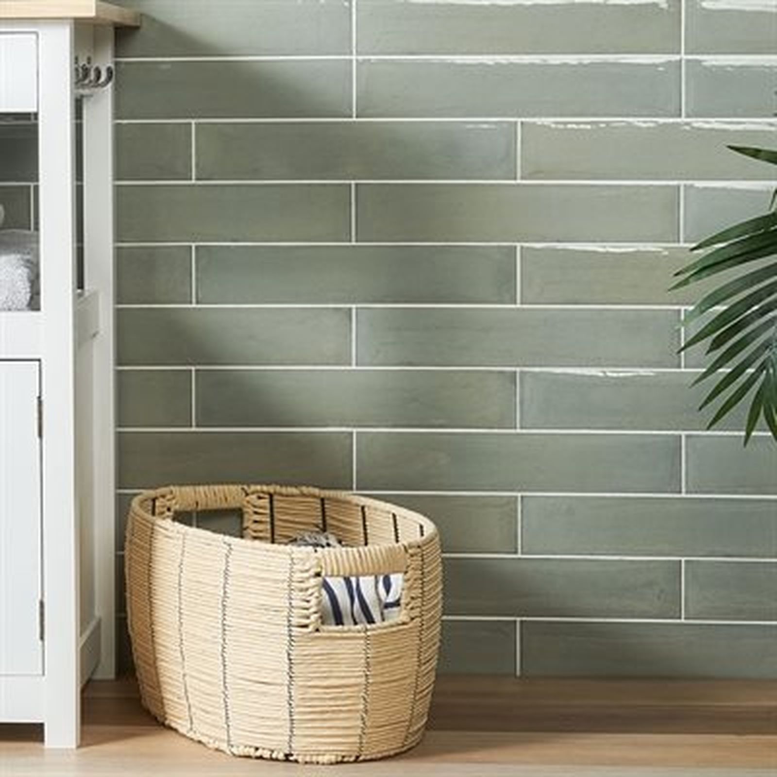 Green tiled wall, woven basket, and a cabinet in a bathroom setting.