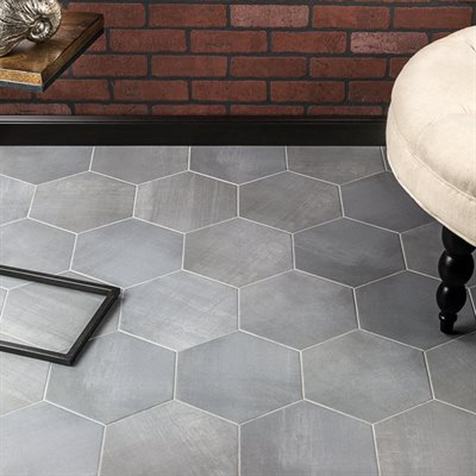 Gray hexagonal tiles on a floor, with a brick wall, table, and a cushioned stool.