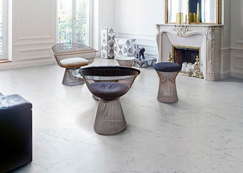 A bright living room with modern wire furniture on a marble floor, and a fireplace in the background.