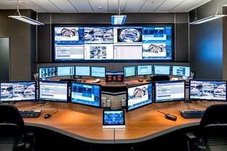 Una sala de control llena de muchos monitores de computadora y una pantalla grande.