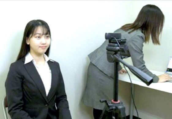 Una mujer con traje está sentada frente a una cámara.