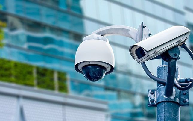 Dos cámaras de seguridad están montadas en un poste frente a un edificio.