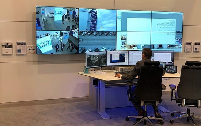 Un hombre está sentado en un escritorio frente a una pantalla grande.