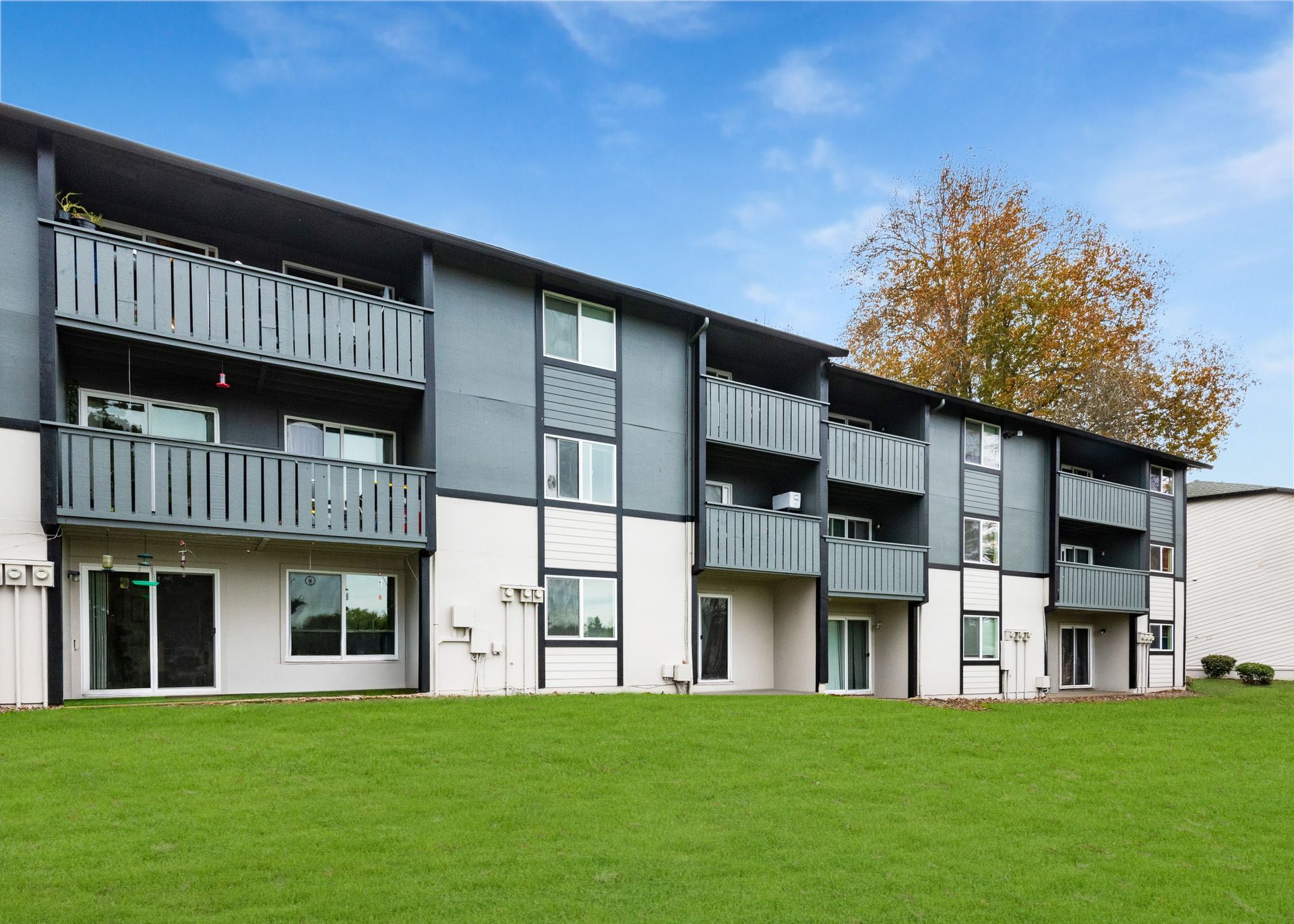 Exterior view of a multi-story apartment building with balconies and a green lawn.