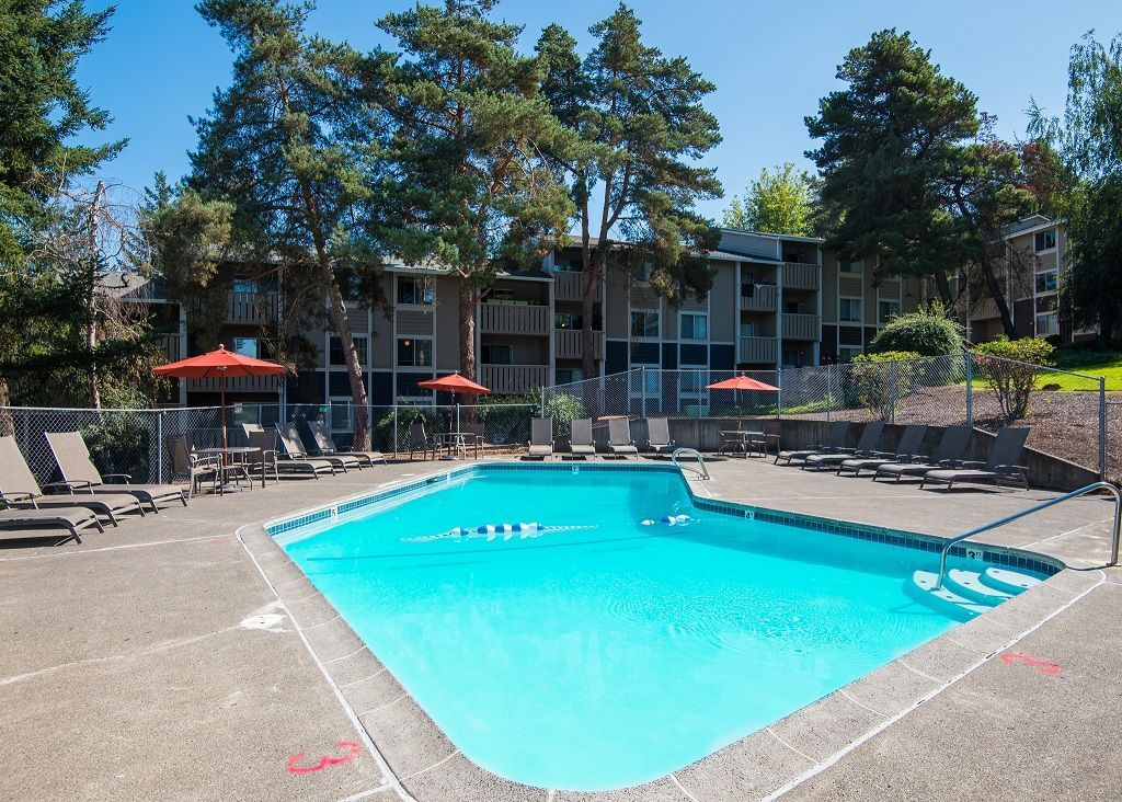 Outdoor apartment community pool with lounge chairs and red umbrellas.