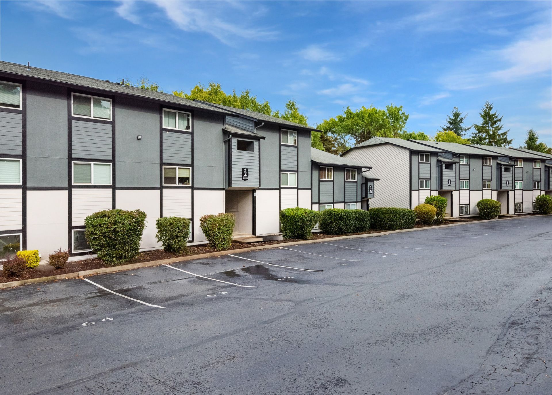 Exterior view of a gray multi-building apartment complex with a parking lot.