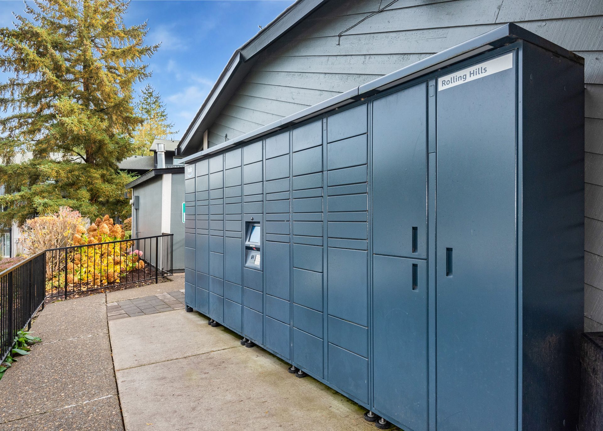 Row of blue outdoor parcel lockers beside an apartment building.
