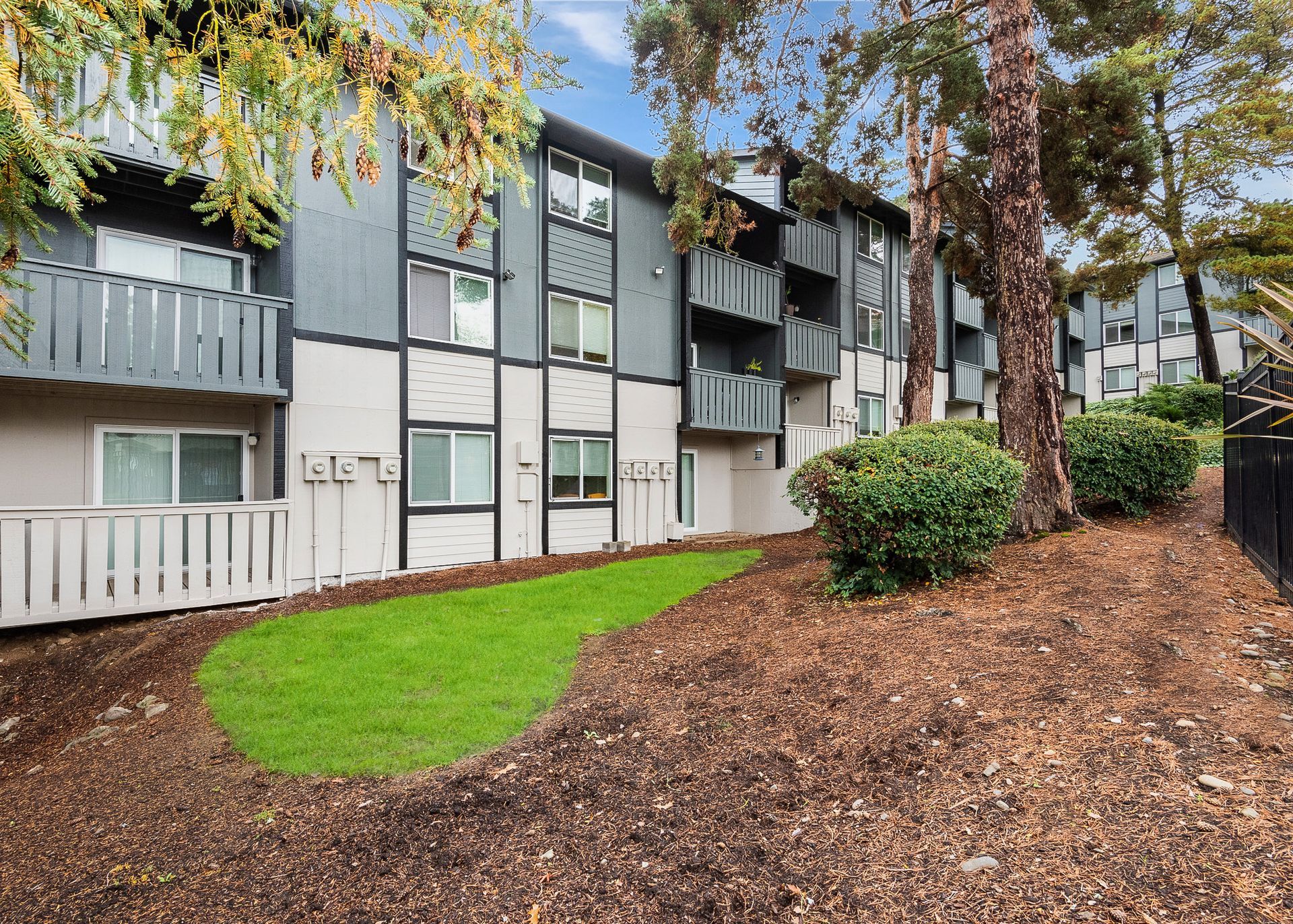 Exterior view of a multi-unit apartment building with small balconies and surrounding trees.