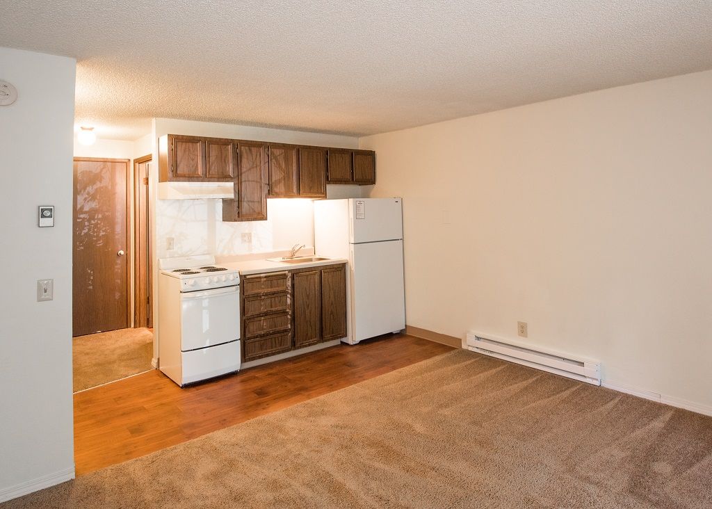 Compact apartment kitchen with dark wood cabinets, white stove and refrigerator, adjacent living area.
