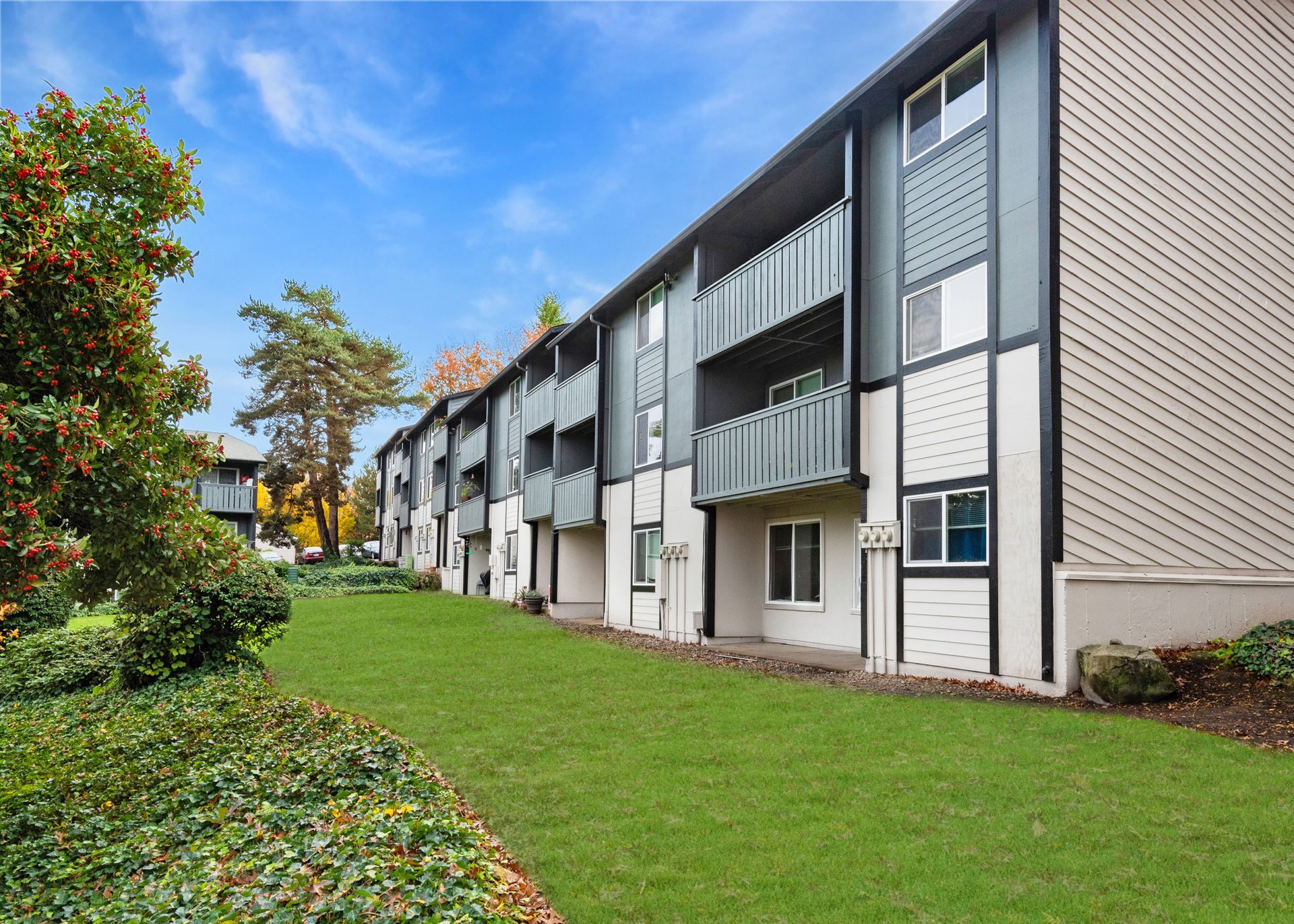 Exterior view of a modern apartment building with balconies and green lawn under a blue sky.