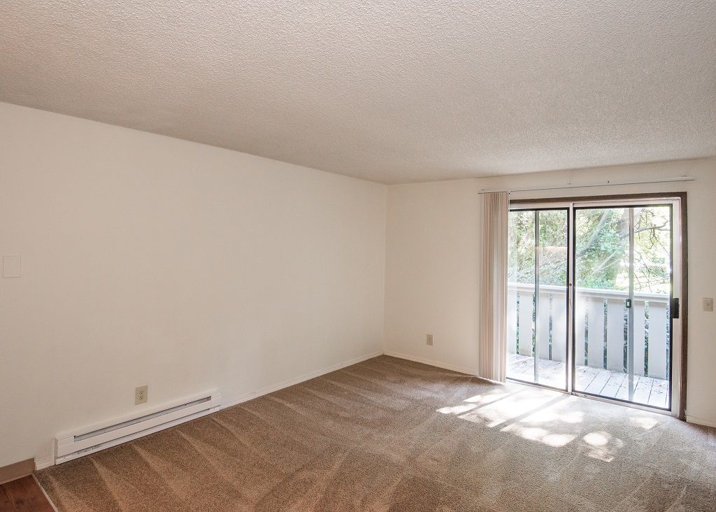 Living room in an apartment with beige carpet, white walls, and a sliding glass door to a balcony.