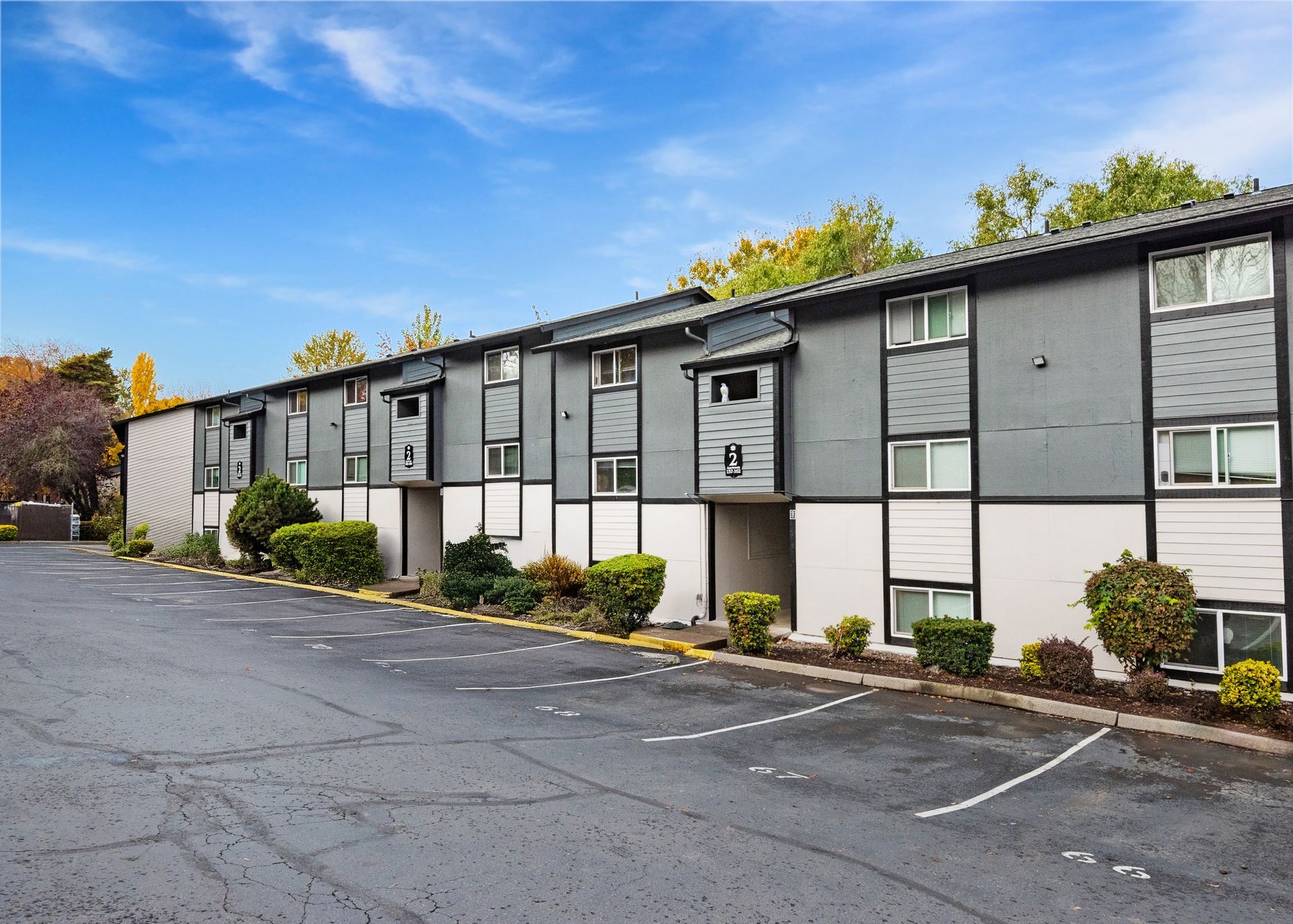Exterior view of a gray, multi-building apartment complex with a parking lot.