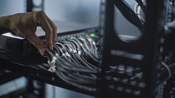 A hand organizing multiple black Ethernet cables plugged into a network server rack.