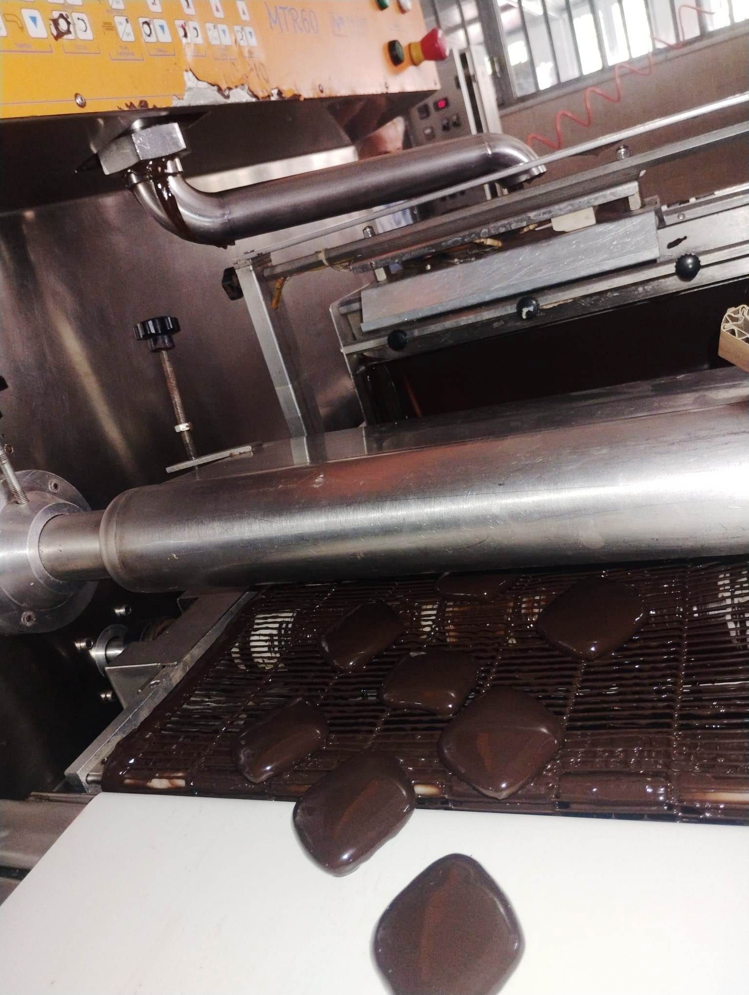 Macchina che deposita dolcetti ricoperti di cioccolato su un nastro trasportatore in fabbrica.