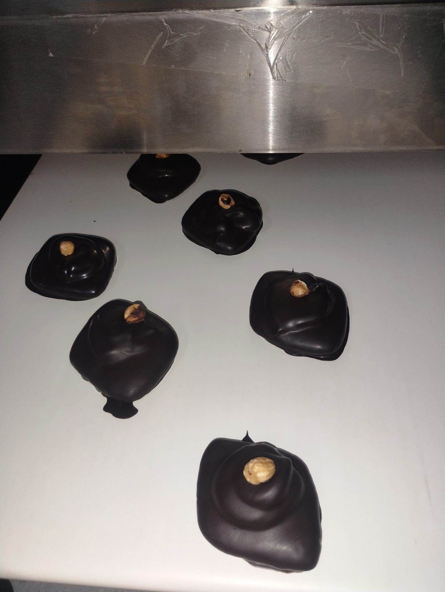 Caramelle al cioccolato fondente con una nocciola su una superficie bianca.