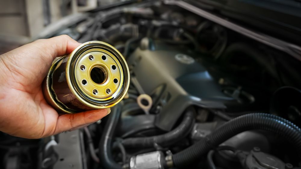 A Person Is Holding a Oil Filter in Front of A Car Engine — Top End Diesel In Palmerston, NT
