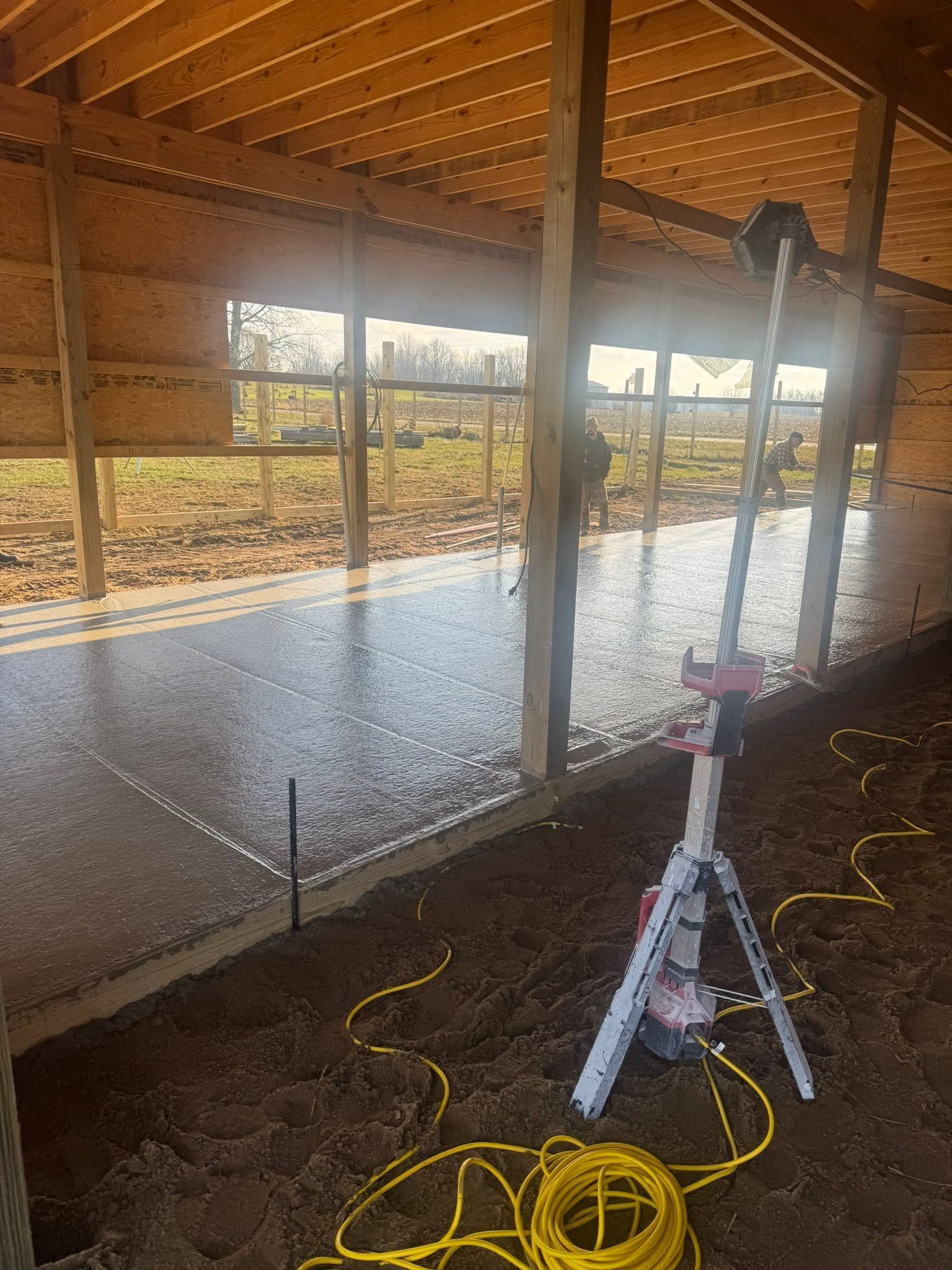 Water flowing in a covered barn aisle, with a tripod and yellow hose in the foreground.